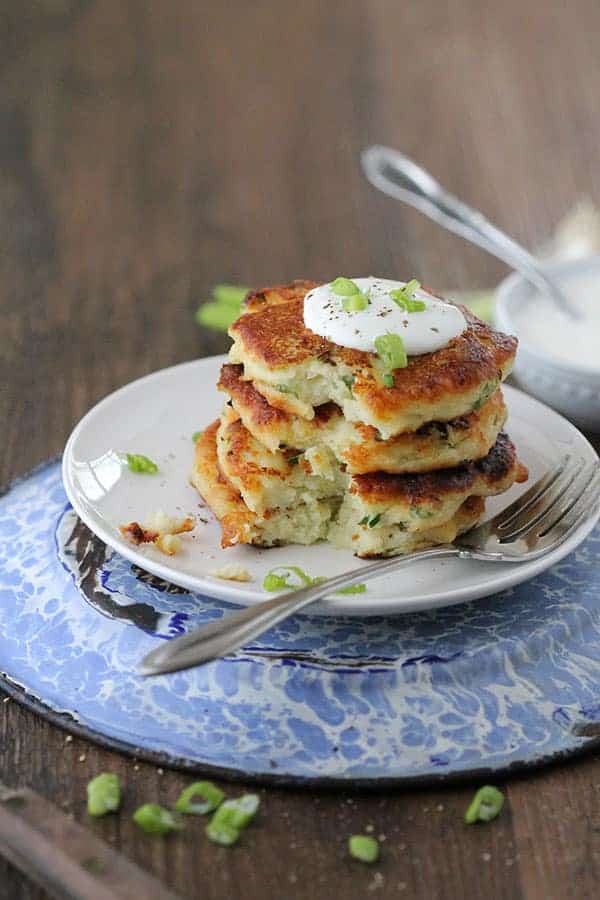 a stack of crispy potato cakes with a bite missing on a small white plate on a blue dish with a fork