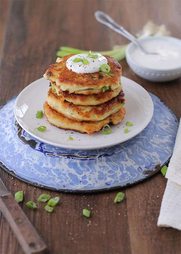 a stack of crispy potato cakes with sour cream on top on a small white plate on a blue dish