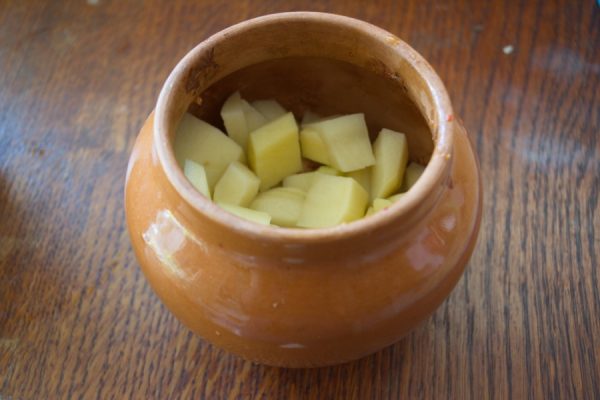 Нарезанный кубиками сырой картофель в керамическом горшочке с мясом