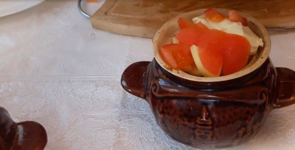 Керамический горшочек с кусочками помидора и репчатого лука на столе