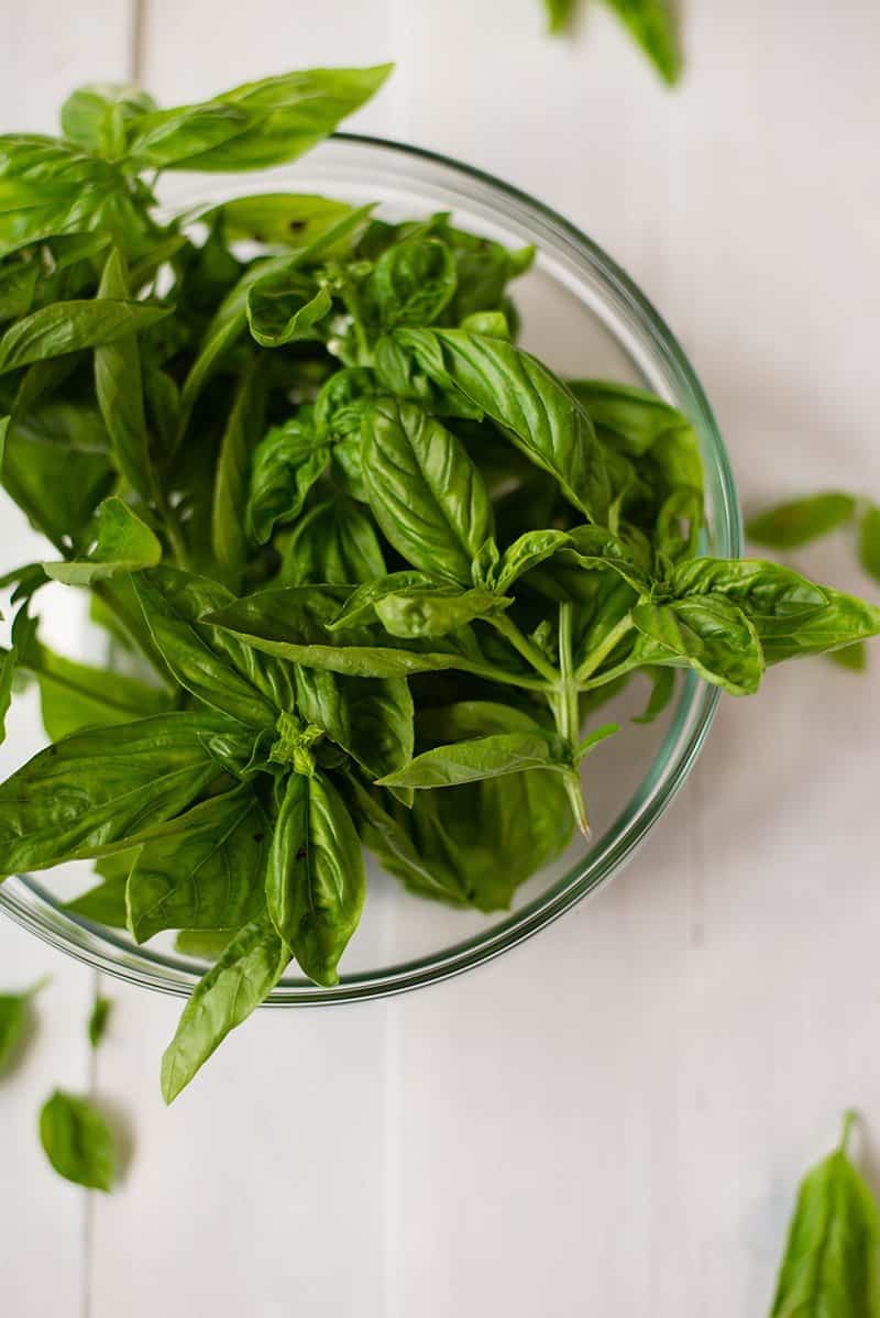Overhead view of fresh basil leaves in a glass bowl.