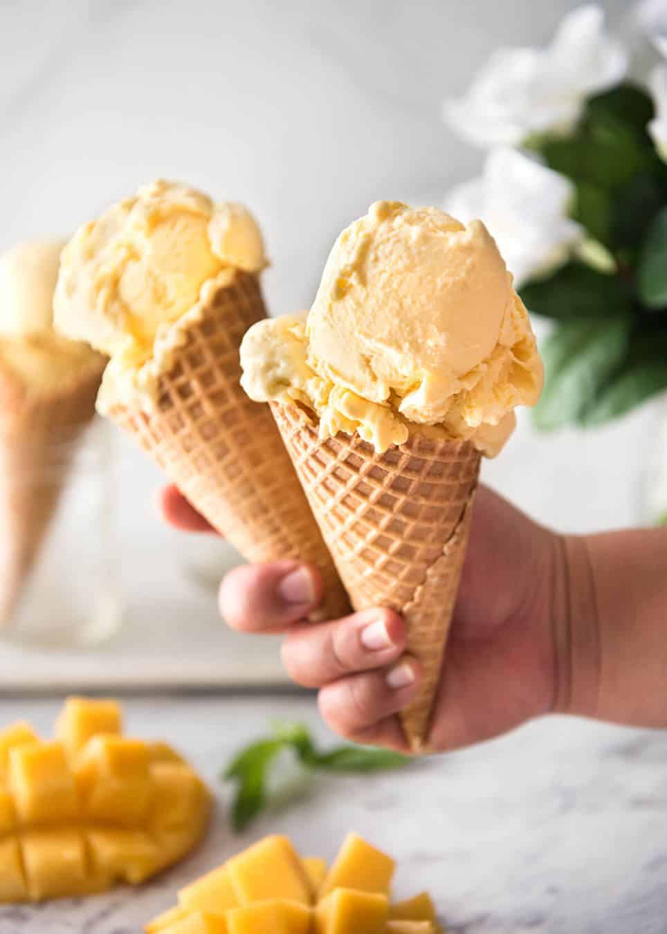 Two ice cream cones with mango ice cream held in a hand.