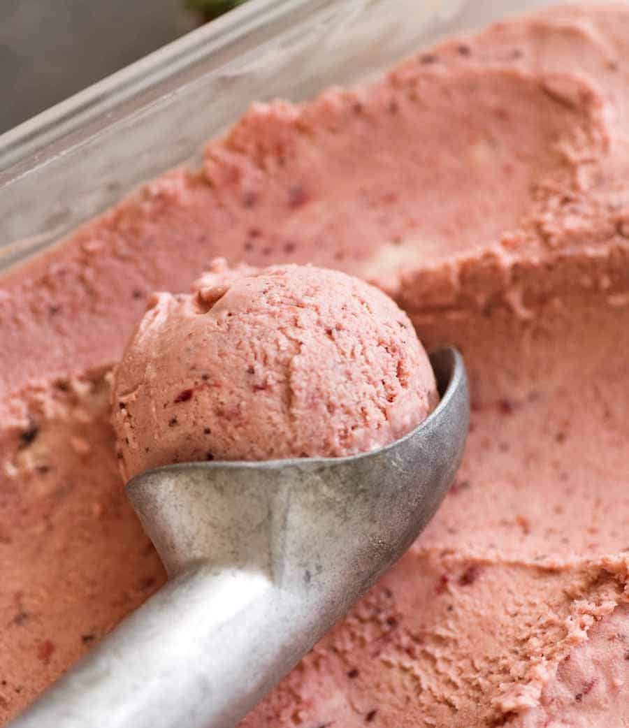 Close up of Creamy No Churn Strawberry Ice Cream in a glass dish being scooped with an ice cream scooper